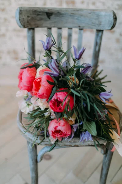 Rustic wedding bouquet with white roses and crimson peonies on the aged gray wooden chair. Indoors. — Stock Photo, Image