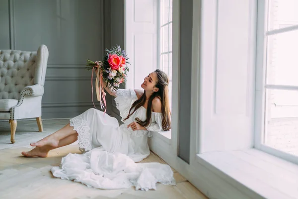 Cheerful, young bride holds a rustic wedding bouquet with peonies on panoramic window background. Close-up portrait. A happy brunette girl with a bunch of flowers. — Stock Photo, Image