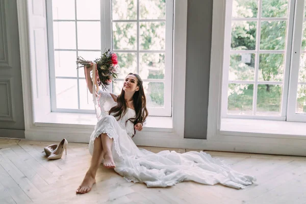 Joyeux, jeune mariée tient un bouquet de mariage rustique avec des pivoines sur fond de fenêtre panoramique. Portrait en gros plan. Une fille brune heureuse avec un bouquet de fleurs . — Photo