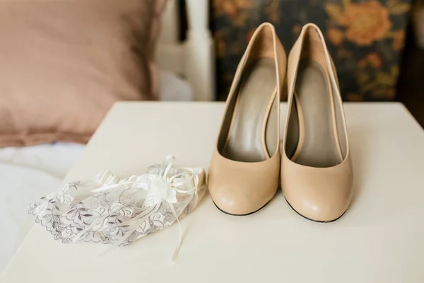 Chaussures beiges sur talons et jarretière en dentelle sur une table blanche. Préparation du mariage. Oeuvres — Photo