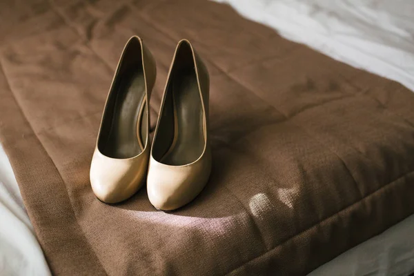 Zapatos beige en los talones de una novia sobre un fondo textil marrón. Preparación de boda. Obra de arte . — Foto de Stock