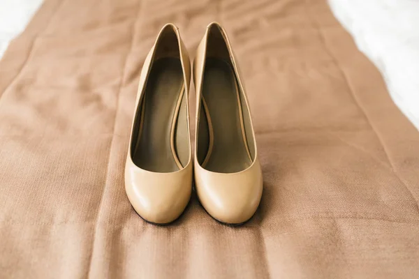 Zapatos beige en los talones de una novia sobre un fondo textil marrón. Preparación de boda. Obra de arte . — Foto de Stock