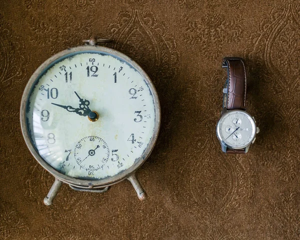 Vintage table clock and mans wristwatch on a brown background. Artwork — Stock Photo, Image