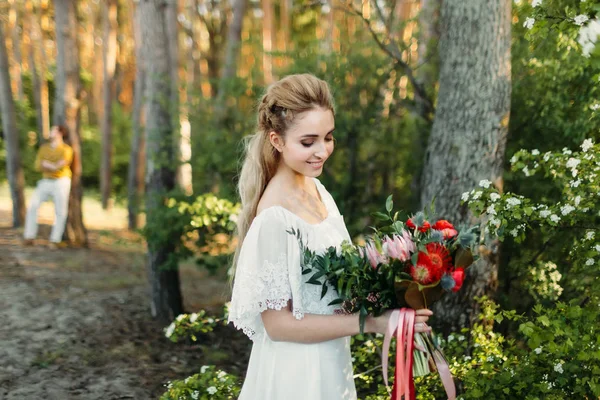 Young blonde bride with a rustic bouquet is posing outdoor in the park. Artwork. Autumn wedding ceremony outdoors. — Stock Photo, Image