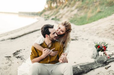 Genç bir çift gülümseyen ve sahilde sarılma. Güzel kız sevgilisini arkadan kucaklamak. Düğün yürüyüş. Sanat