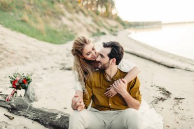 Genç bir çift gülümseyen ve sahilde sarılma. Rustik düğün töreni açık havada. Gelin ve damat birbirlerine şefkat ve sevgi ile bakıyorlar. Sanat