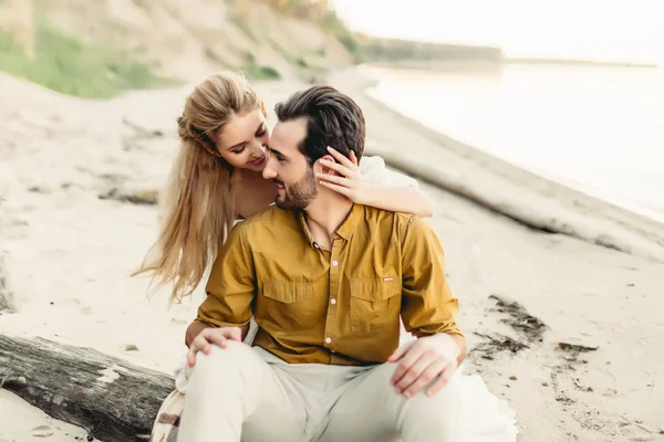 Una pareja joven se está divirtiendo y abrazando en la playa. Hermosa chica abrazar a su novio desde atrás. Paseo nupcial. Un recién casado se mira el uno al otro. Obra de arte — Foto de Stock