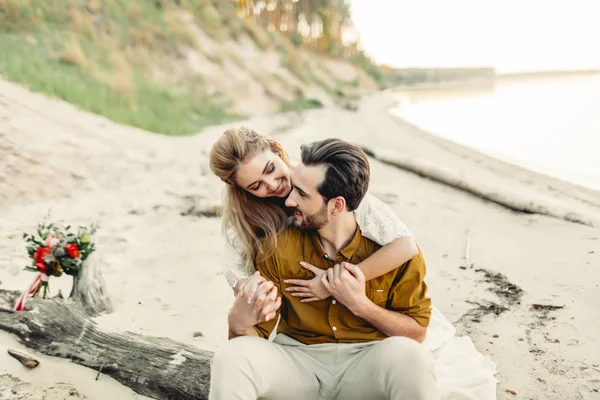 A young couple is smiling and hugging on the beach. Rustic wedding ceremony outdoors. Bride and groom look at each other with tenderness and love. Artwork — Stock Photo, Image