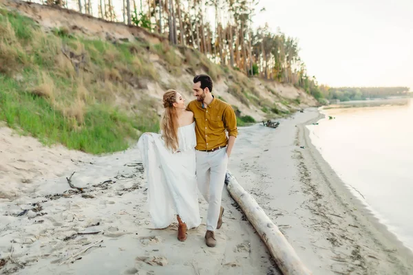 A young couple is having fun and walking on the sea coastline. Newlyweds looking at each other with tenderness. Romantic date on the beach. Wedding. Artwork — Stock Photo, Image