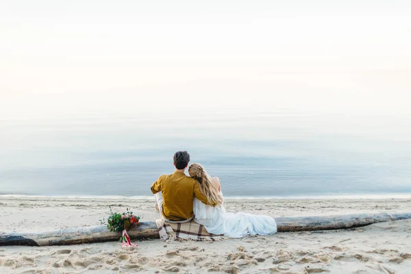 Un beau couple est assis sur la bûche et regarde vers la mer. Rendez-vous romantique sur la plage. Vue de l'arrière. Mariage. Oeuvres — Photo