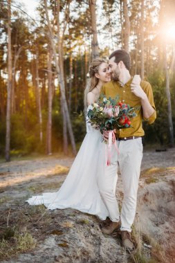 Güzel gelin onun damat tarafından omuz kucaklar. Bir ormandaki düğün yürüyüş. Yeni evli birbirine benziyor. Kız beyaz elbise ve bir zeytin tişörtlü adam. Sanat.