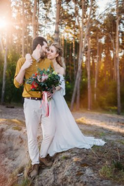 Güzel gelin onun damat tarafından omuz kucaklar. Bir ormandaki düğün yürüyüş. Yeni evli birbirine benziyor. Kız beyaz elbise ve bir zeytin tişörtlü adam. Sanat.