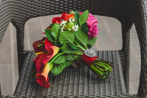 Hochzeitsstrauß mit leuchtend roten Blumen und Band mit einer silbernen Brosche am Stiel. Nahaufnahme. Kunstwerk — Stockfoto