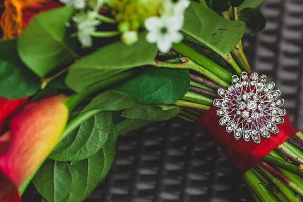 Um broche de prata com strass no talo do buquê de casamento com fitas vermelhas. Close-up. Obra de arte — Fotografia de Stock