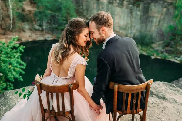 Recém-casados sentados à beira do desfiladeiro e casal olhando uns para os outros com ternura e amor. Noiva e noivo a tocar nas testas. Casamento — Fotografia de Stock