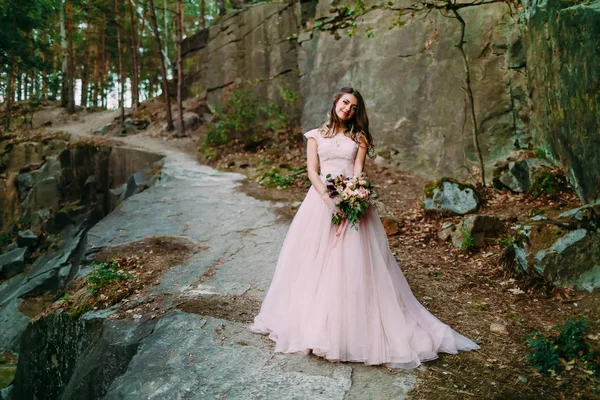 Bride with rustic wedding bouquet stands on the rock — Stock Photo, Image