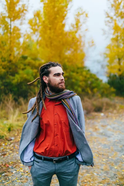 Hipster. Um homem elegante com dreadlocks e barba em uma camisa vermelha e casaco cinza. Brilho posando sobre a natureza. Cerimônia de casamento outono ao ar livre . — Fotografia de Stock