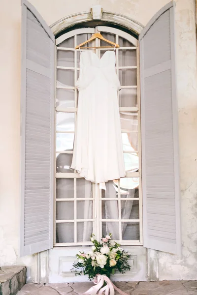 Een witte bruids jurk op houten schouders, tegen het raam. Illustraties — Stockfoto