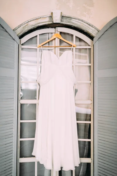 Ein weißes Brautkleid auf hölzernen Schultern, vor dem Fenster. Kunstwerk — Stockfoto