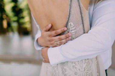 Damat kucaklama kadın tarafından bel. Sanat. Yumuşak odak. Bej uydurma elbise ve Beyaz gömlekli damat güzel tabaklanmış gelin. Açık havada