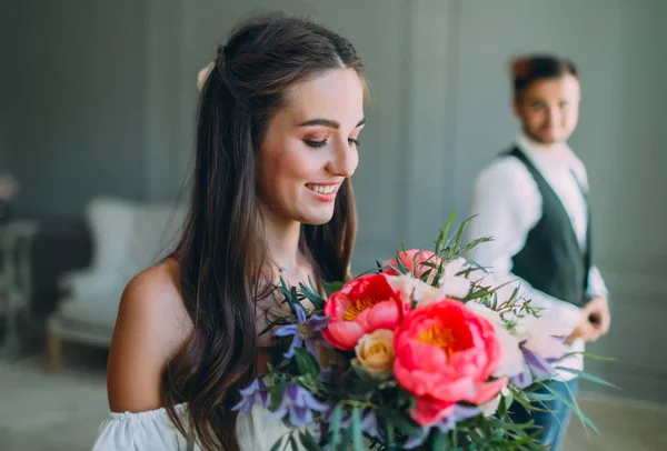 Närbild porträtt av glada, unga bruden med en brudbukett på suddig brudgummen bakgrund. En glad tjej med en massa blommor — Stockfoto