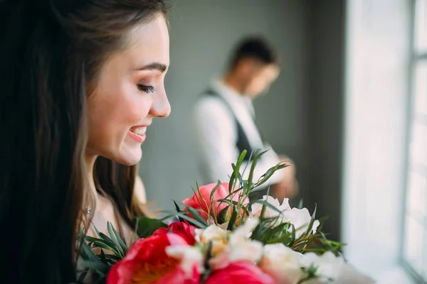 Крупним планом портрет веселої молодої нареченої з весільним букетом на розмитому фоні нареченого. Щаслива дівчина з купою квітів — стокове фото