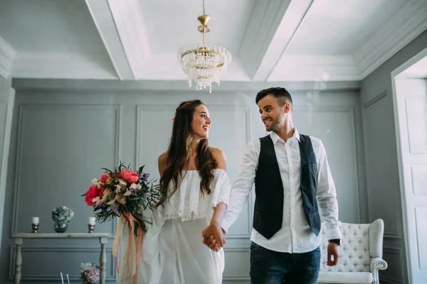 Novia alegre y novio tomados de la mano. Recién casados riéndose y mirándose. Obras de arte. Boda en interiores. Enfoque suave —  Fotos de Stock