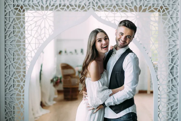 Una novia alegre y el novio con una linda sonrisa riendo y abrazando. Hermosos recién casados posando en habitación vintage — Foto de Stock