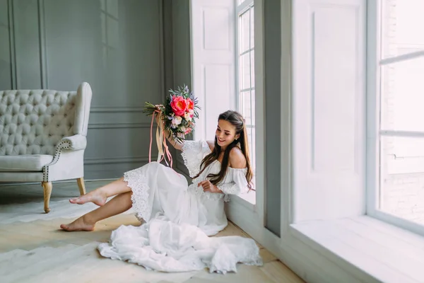 Joven novia alegre sostiene un ramo de boda rústico con peonías en el fondo panorámico de la ventana. Retrato de cerca. Una morena feliz con un ramo de flores . — Foto de Stock