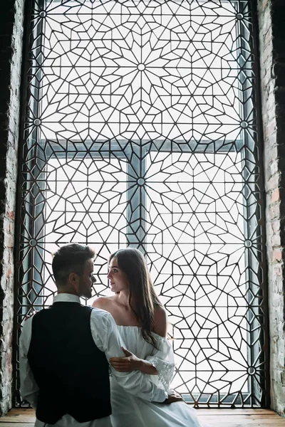 Hermosos recién casados jóvenes están posando en el fondo de la ventana de la vendimia ornamento. Bajo perfil. Obras de arte. Boda — Foto de Stock