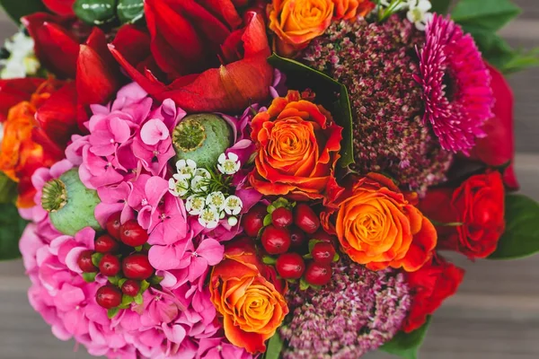Романтичний весільний букет з помаранчевими, малиновими та бордоськими трояндами, маком та іншими квітами та зеленню на дерев'яному фоні. Крупним планом . — стокове фото