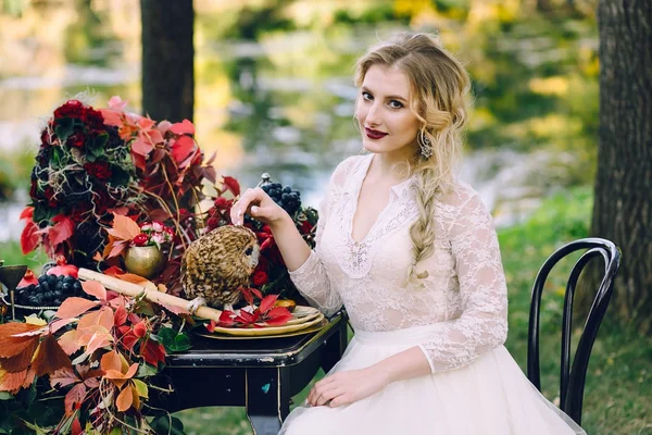 La novia con el búho. Hermosa novia sonriente está sentada cerca de la mesa de bodas servida con hojas rojas de otoño — Foto de Stock