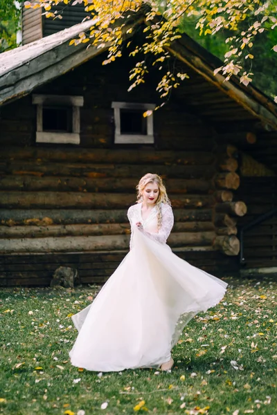 La hermosa novia está girando alrededor de sí misma en vestido revoloteando sobre el fondo de la casa de madera. Obra de arte — Foto de Stock