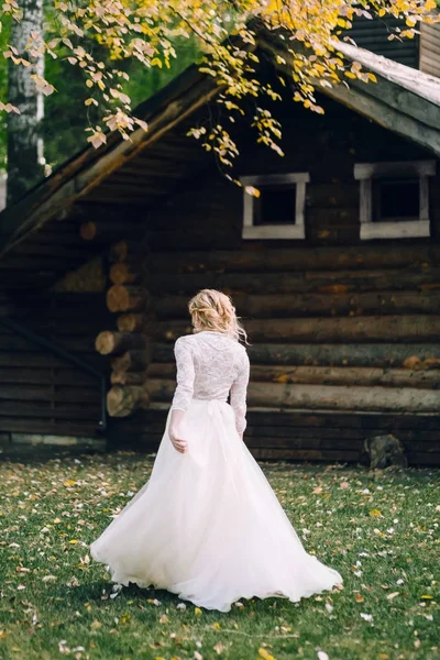 Novia rubia está caminando en vestido revoloteando sobre fondo de casa de madera. Vista trasera. Obra de arte — Foto de Stock