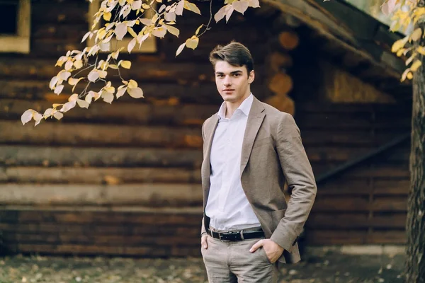英俊的新郎站在木屋旁边。秋季婚礼户外 — 图库照片