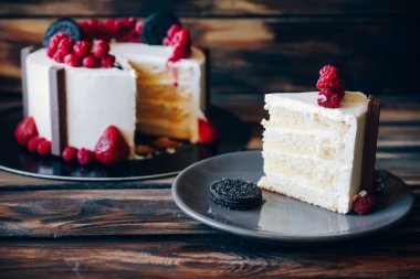 Slice of cake topped with strawberries and chocolate cookies on the wooden background. Artwork.
