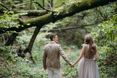 Mutlu bir çift, bir sonbahar ormanındaki bir iz üzerinde yürüyor. Gelin ve damat birbirlerine doğa üzerinde arıyoruz.