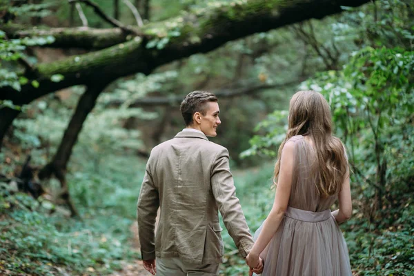 Счастливая пара идет по тропе в осеннем лесу. Жених и невеста смотрят друг на друга на природе . — стоковое фото