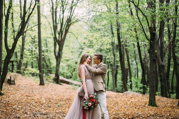 Ein glückliches Paar spaziert auf einem Wanderweg in einem herbstlichen Wald. Braut und Bräutigam schauen sich in der Natur an. — Stockfoto