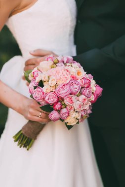 Güzel gelin düğün buket pembe Gül ve peonies ile tutar. Damat kucaklama kadın tarafından bel. Yumuşak odak üstünde çiçekler