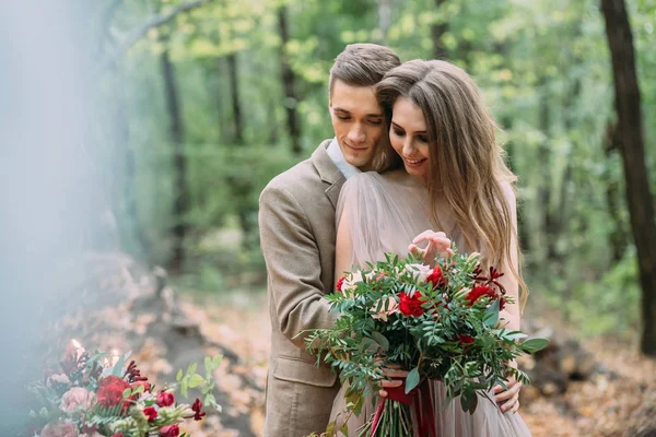 Жених нежно обнимает свою прекрасную невесту сзади. Осенняя свадьба на открытом воздухе. Счастливых молодоженов. — стоковое фото