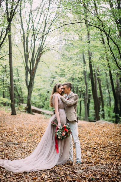 Una pareja feliz está caminando por un sendero en un bosque de otoño. La novia y el novio se miran en la naturaleza . — Foto de Stock