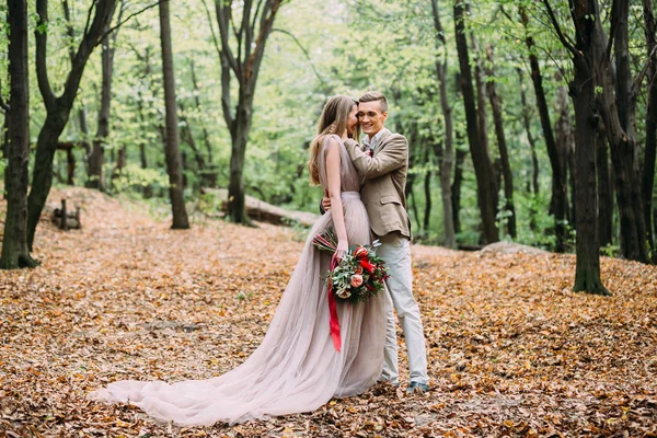 Ein glückliches Paar spaziert auf einem Wanderweg in einem herbstlichen Wald. Braut und Bräutigam schauen sich in der Natur an. — Stockfoto