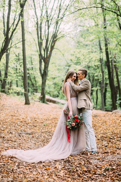 Una pareja feliz está caminando por un sendero en un bosque de otoño. La novia y el novio se miran en la naturaleza . — Foto de Stock