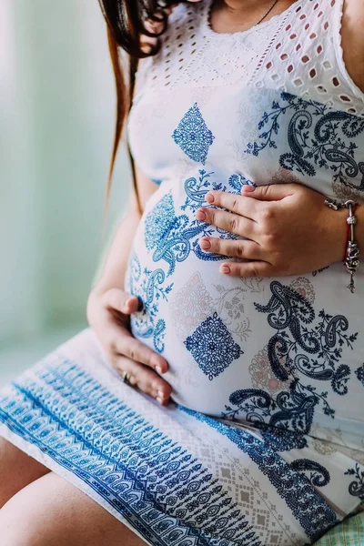 Una mujer embarazada vestida de blanco con adorno toca su vientre. Obras de arte. Primer plano . —  Fotos de Stock