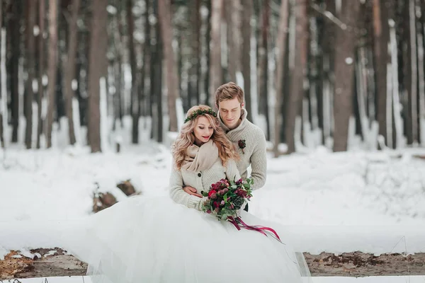 La novia y el novio están sentados en el tronco en el bosque de invierno. Primer plano. Ceremonia de boda . — Foto de Stock