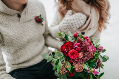 Gelin ve damat sıcak kış giysileri içinde kırmızı ve koyu kırmızı çiçekli bir rustik düğün buket elinde tutar. Yakın çekim.