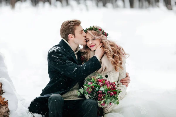 Ženich líbá svou nevěstu na chrámu na pozadí bílého sněhu. Umělecká díla. Selektivní fokus na kytice — Stock fotografie