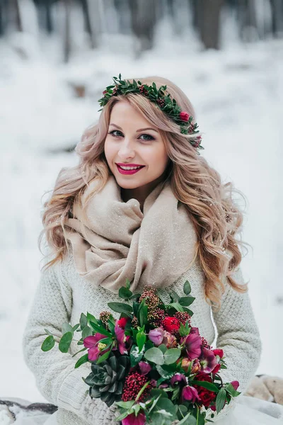 Lächelnde Braut slawischen Aussehens mit einem Kranz aus Wildblumen hält einen Strauß Winterhintergrund. Winterhochzeit — Stockfoto