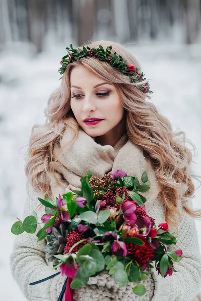 Ein junges Mädchen slawischen Aussehens mit einem Kranz aus Wildblumen. schöne Braut hält einen Strauß im winterlichen Hintergrund. — Stockfoto